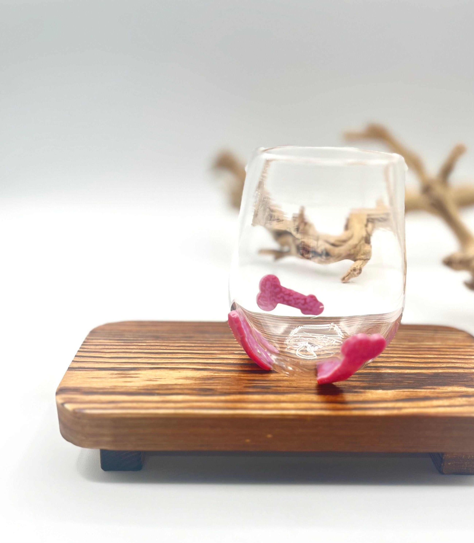 Hand blown stemless wine glass with pink glass penis designs on wooden tray