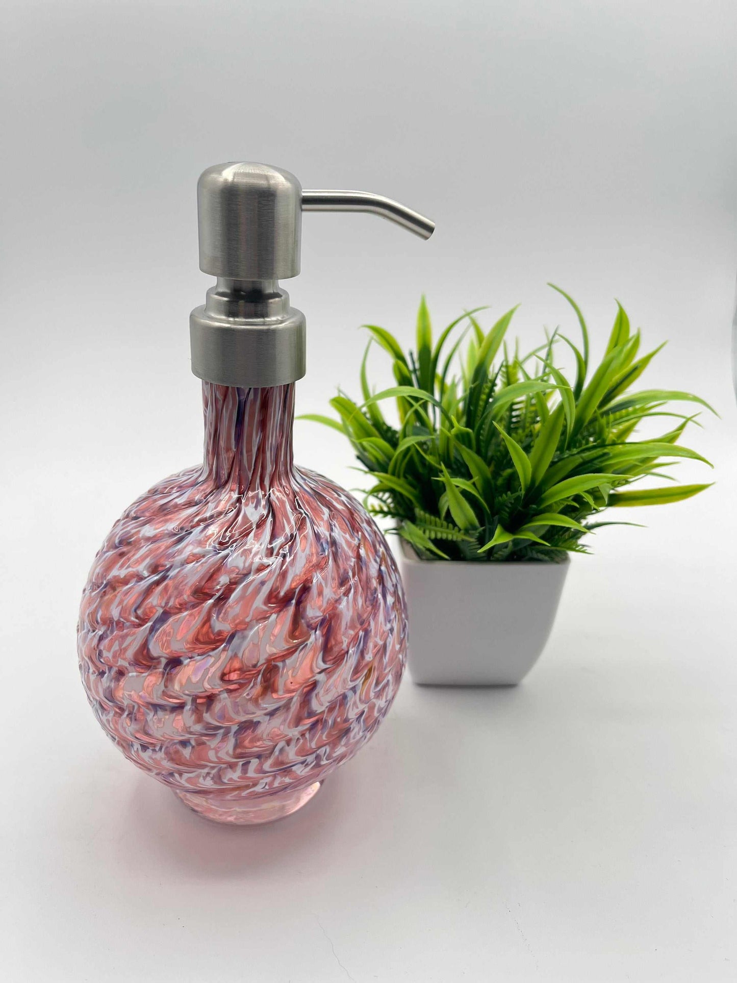 RubyAmethyst Mix marbled hand blown glass soap dispenser with metal pump and textured design next to a small green plant