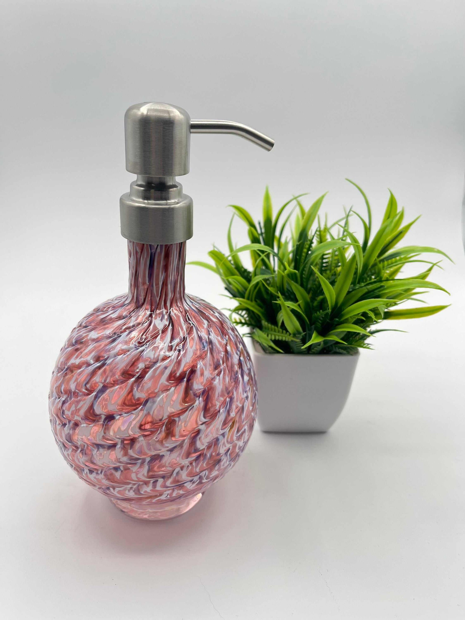 RubyAmethyst Mix marbled hand blown glass soap dispenser with metal pump and textured design next to a small green plant