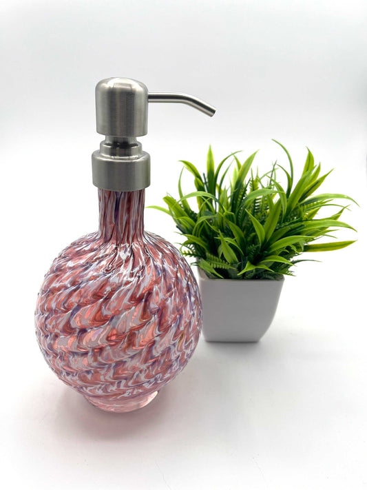 RubyAmethyst mix marbled hand blown glass soap dispenser with stainless steel pump next to small green plant in white pot