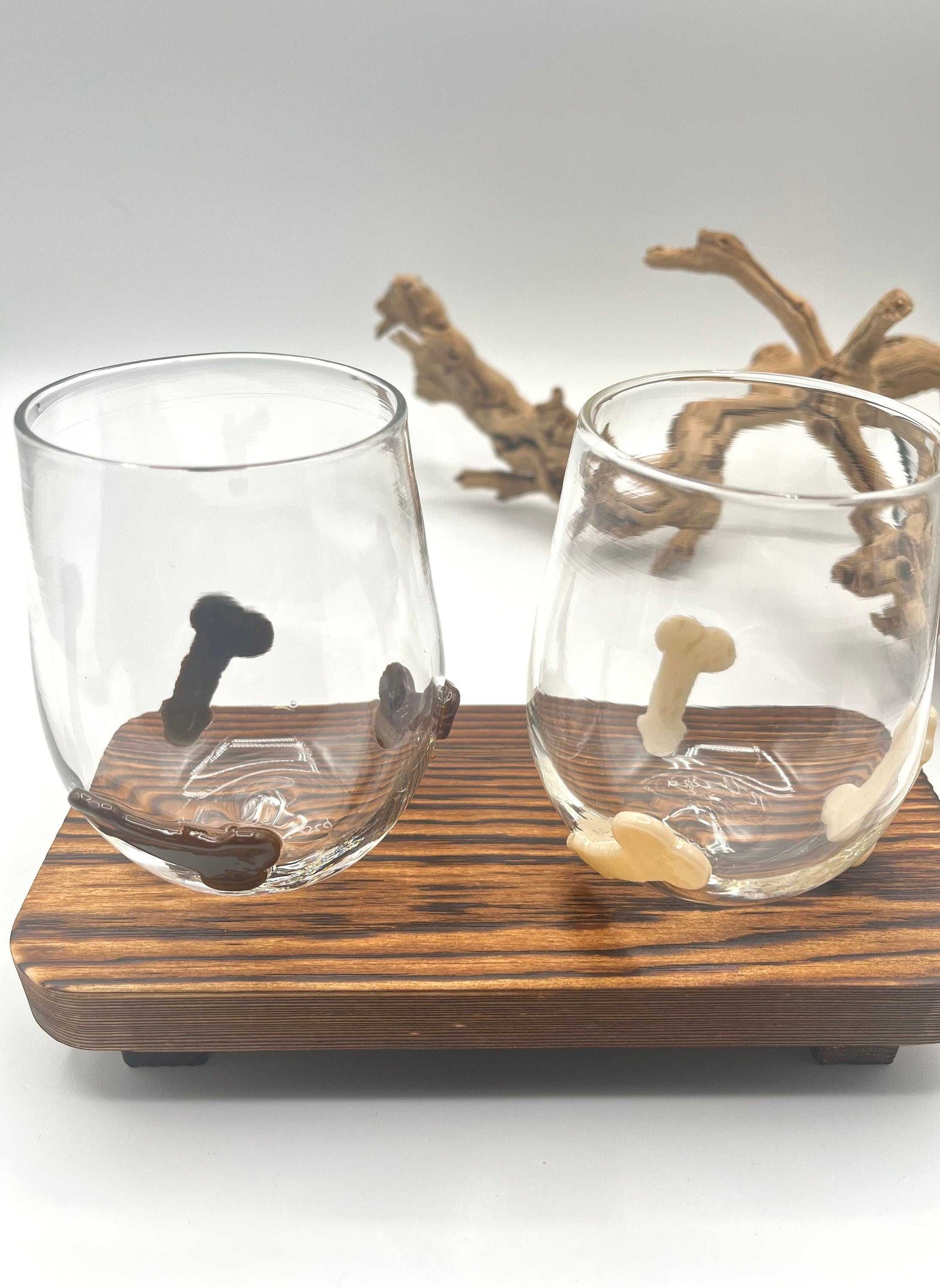 Hand blown stemless wine glasses with playful penis-shaped glass accents in vanilla and chocolate colors on wooden tray