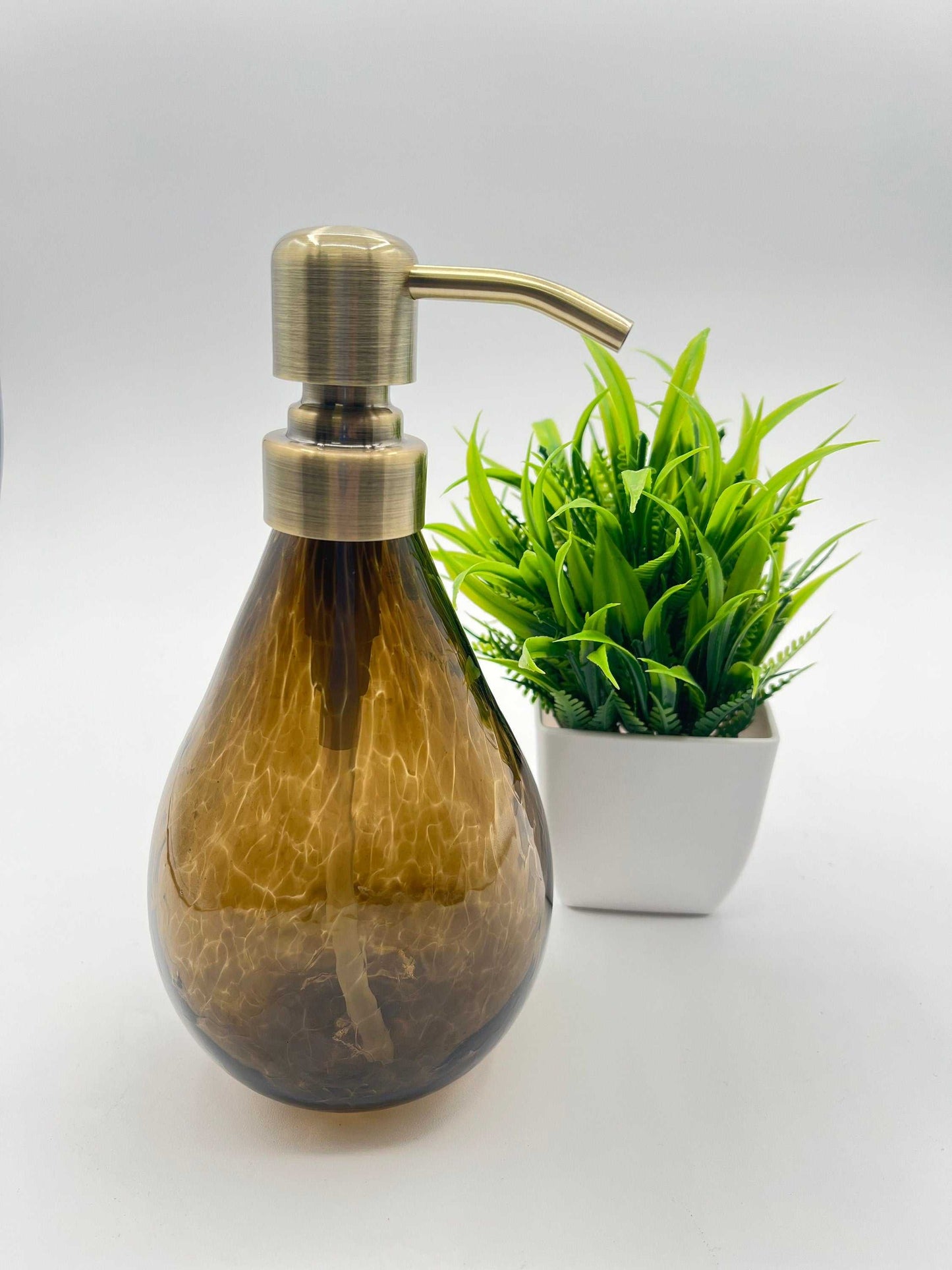 Topaz hand blown glass soap dispenser with brushed metal pump, 12-ounce capacity, next to a small green plant in a white pot
