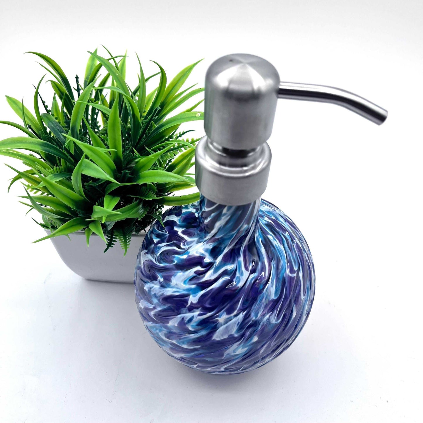 Handblown marbled glass soap dispenser with aqua and hyacinth swirls and stainless steel pump next to green plant in white pot