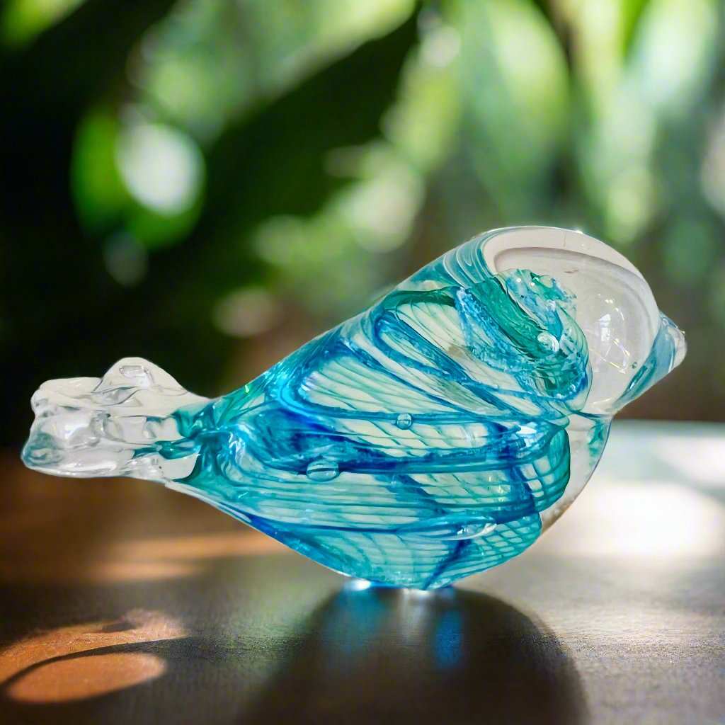 Blue and clear glass memorial healing stone shaped like a bird with intricate swirls, placed on a wooden surface.