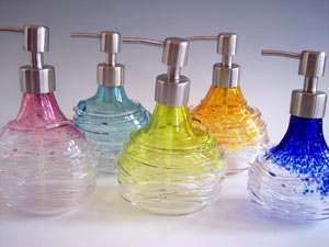 Colorful spun glass soap dispensers with brushed steel pump tops in various hues including ruby, aqua, citron, gold, and blue