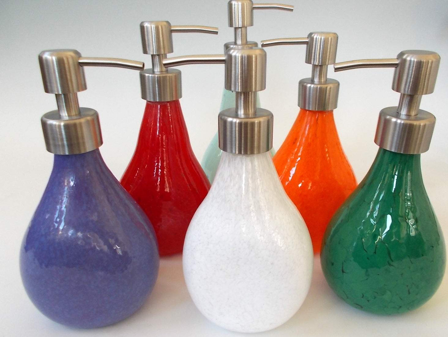 Hand blown solid color soap dispensers with brushed steel pump tops in various colors including purple, red, white, orange, and green
