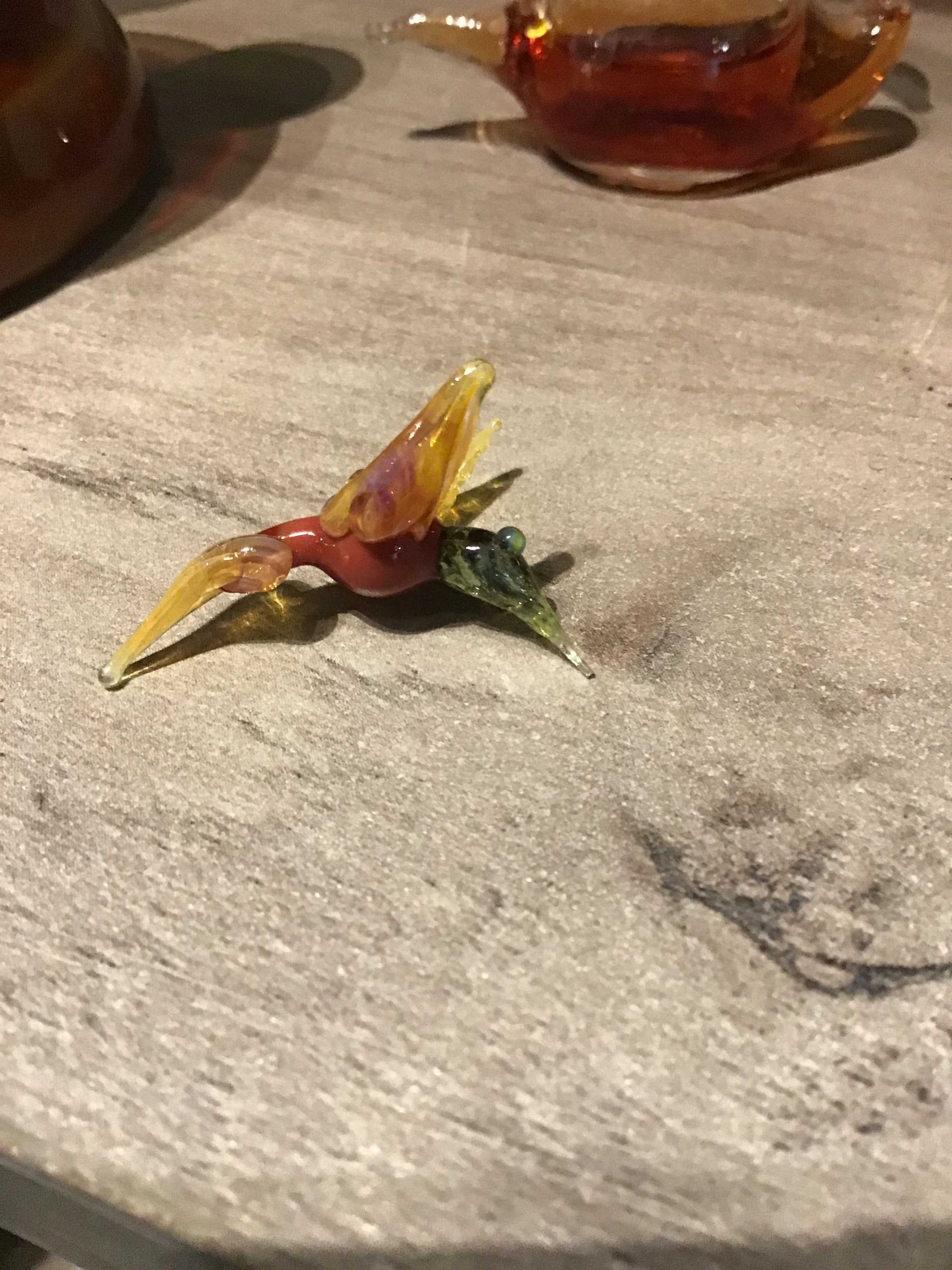 Small colorful glass hummingbird figurine on a textured surface