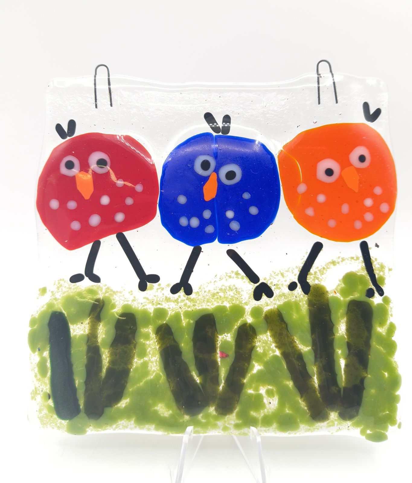 Fused glass art featuring three colorful birds with red, blue, and orange bodies standing on green grass, part of the Choose Your Own Fusing Project class.