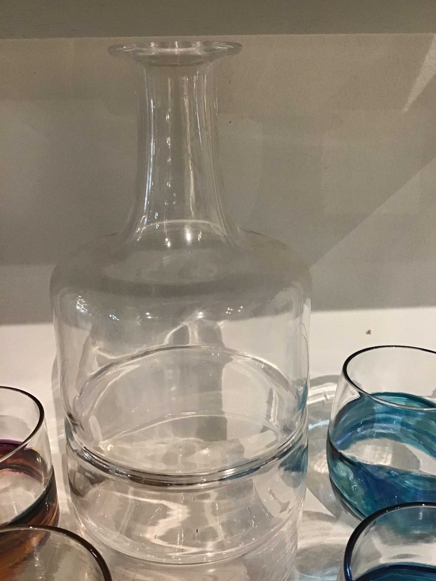 Clear glass bourbon decanter with round base and narrow neck alongside whiskey glasses