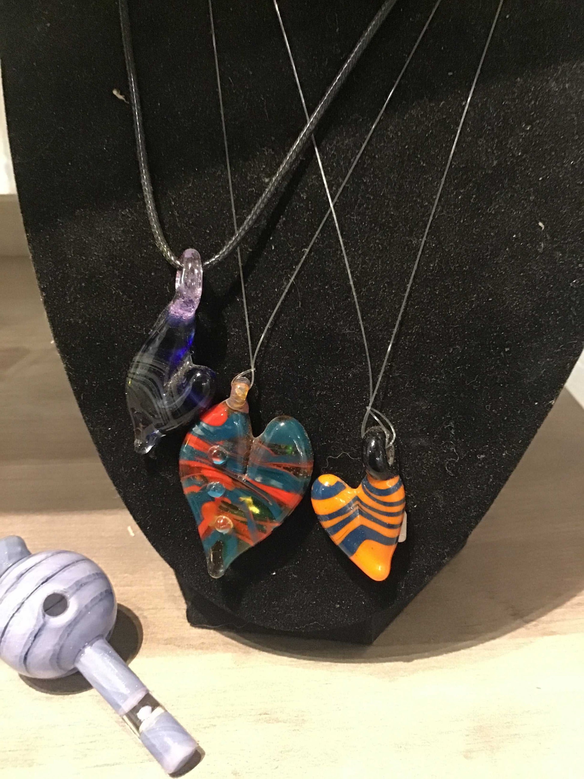 Colorful glass heart pendant necklaces on display with a black background