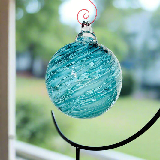 AquaCeledon Optical Glass hand-blown blue glass ornament with swirling design hanging on black stand