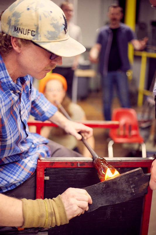 Professional artist demonstrating glassblowing at private glassblowing demo event with attendees watching.