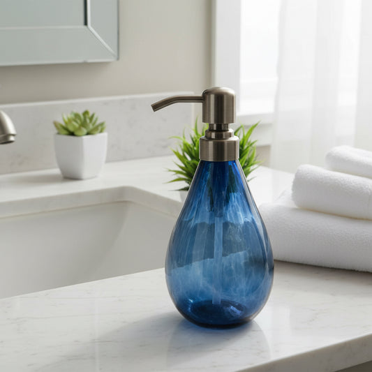 Blue hand blown glass soap dispenser with metal pump and 12-ounce capacity next to small green plant in white pot