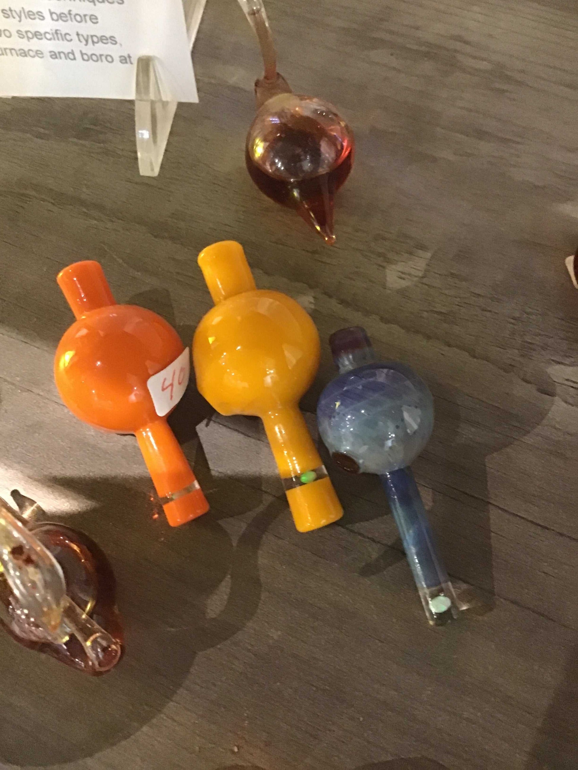 Three colorful baby bong beads in orange, yellow, and blue on a wooden surface