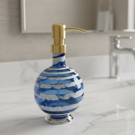 Boho handblown glass soap dispenser in steel blue with distressed white spiral and gold pump next to green plant in white pot