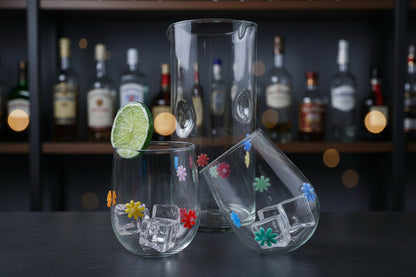 Hand blown stemless wine glasses with colorful retro flower designs and a clear glass pitcher on a wooden tray