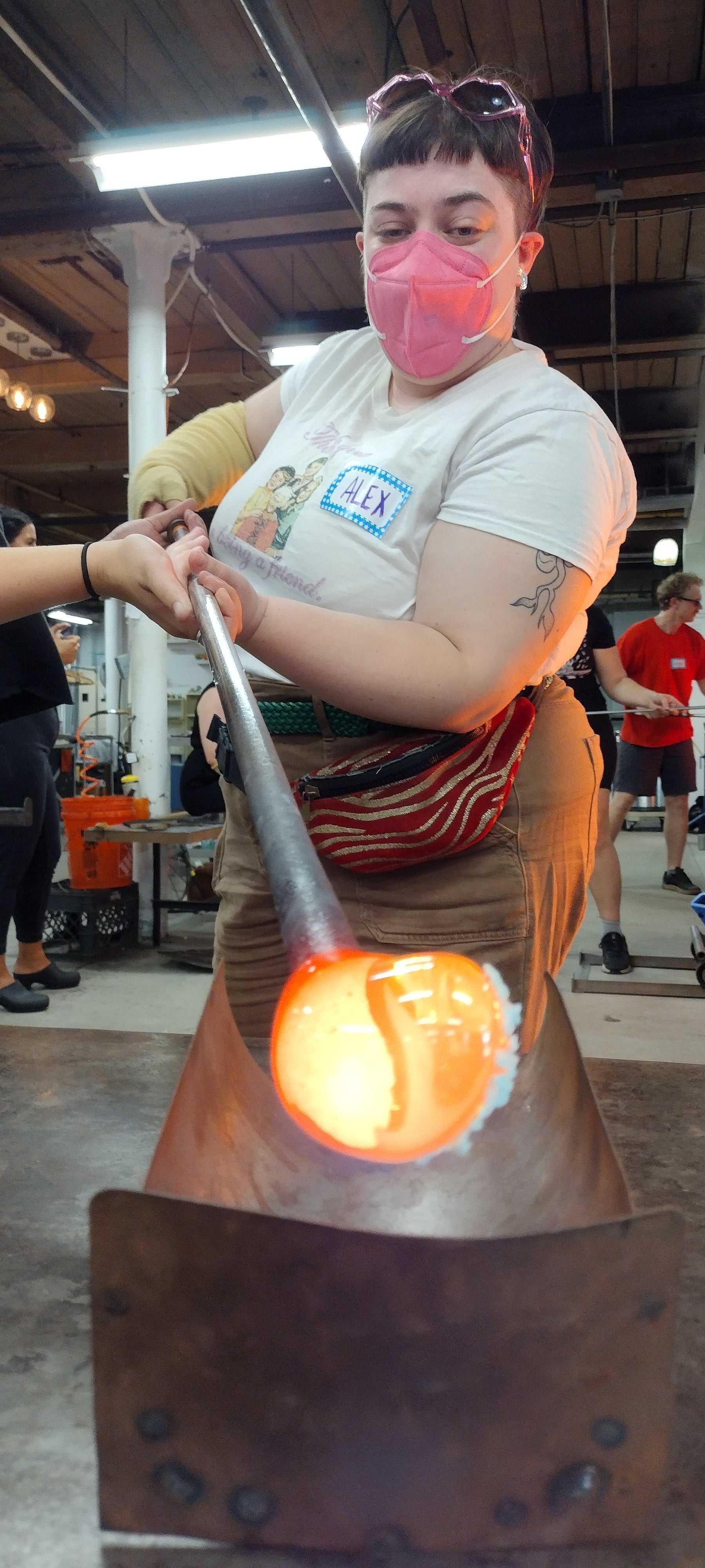 Person shaping molten glass on a blowpipe in a Date Night Glassblowing class studio