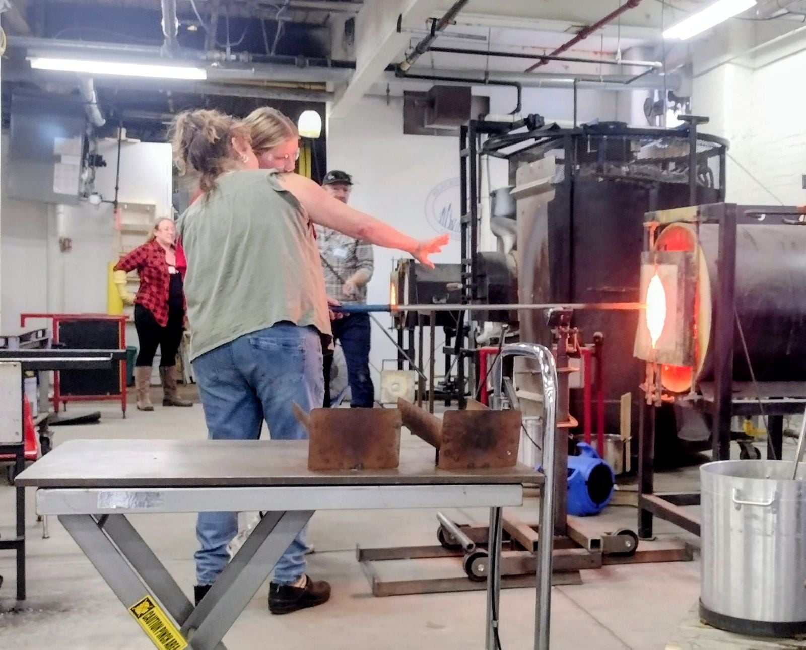 Couple participating in a date night glassblowing class with open kiln and glass tools.