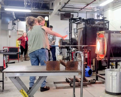 Couple participating in a date night glassblowing class with open kiln and glass tools.