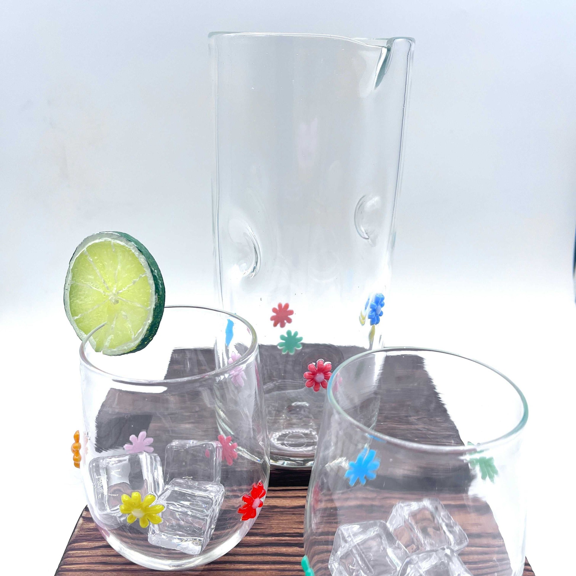 Hand blown stemless wine glasses with colorful flower designs and matching glass pitcher on wooden surface