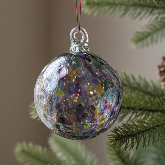 A hand-blown glass Christmas ornament with a clear glass body containing colorful swirls of purple, blue, yellow, and pink, suspended by a thin red string against a neutral gray background.