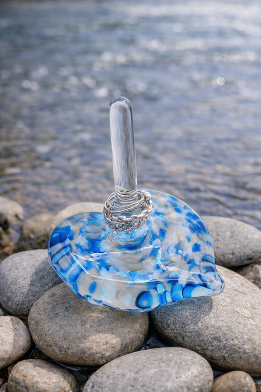 Glass dish with blue and white pattern on pebbles by a water body