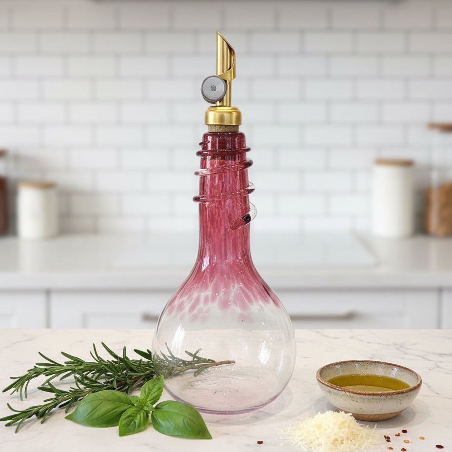 Ruby hand blown Olive Oil & Vinegar Spiral Neck Drizzler Cruet Bottle with weighted gold pour spout on kitchen counter with two green plants