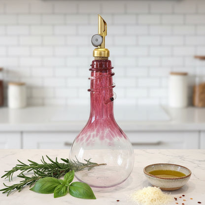 Ruby hand blown Olive Oil & Vinegar Spiral Neck Drizzler Cruet Bottle with weighted gold pour spout on kitchen counter with two green plants
