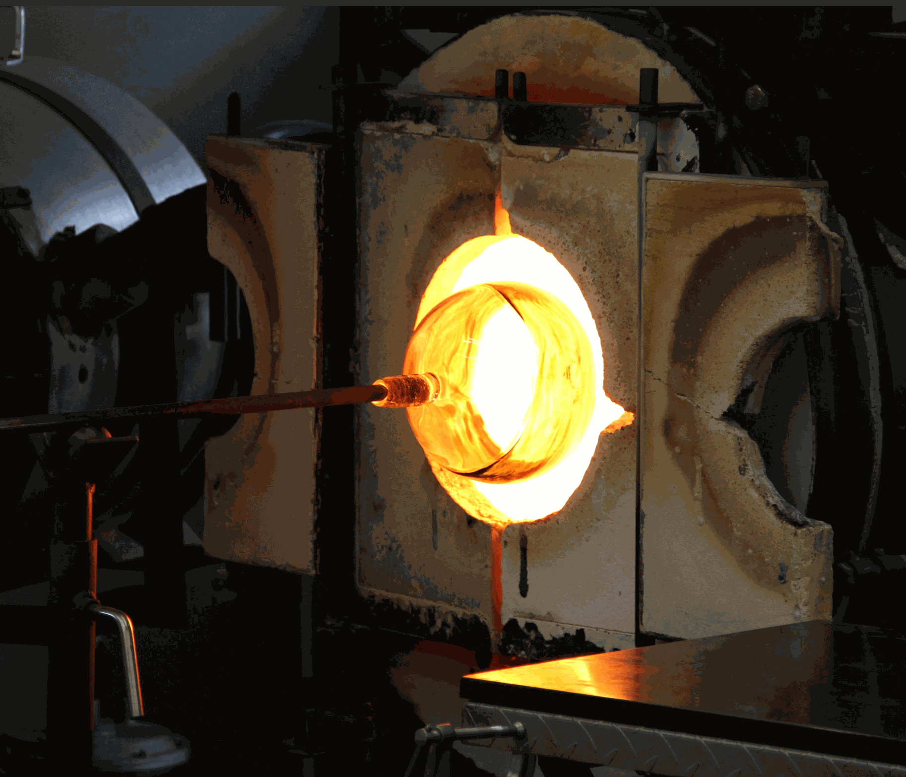 Molten glass being shaped at the end of a pipe inside a glassblowing furnace for make your own ornament workshop.