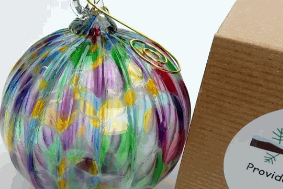 Colorful hand-blown glass ornament with swirling patterns next to a cardboard box labeled "Provid"
