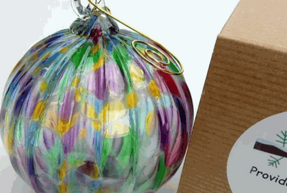 Colorful hand-blown glass ornament with swirling patterns next to a cardboard box labeled "Provid"