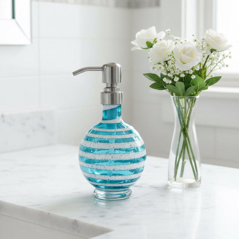 Boho handblown teal blue glass soap dispenser with distressed white spiral and stainless steel pump next to green plant in white pot