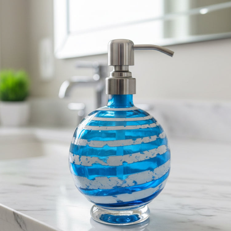 Boho handblown glass soap dispenser in aqua blue with distressed white spiral and stainless steel pump next to green plant in white pot