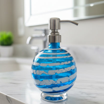 Boho handblown glass soap dispenser in aqua blue with distressed white spiral and stainless steel pump next to green plant in white pot