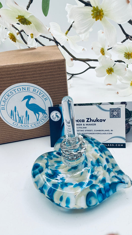Blue and white glass ring holder on a white surface with a Blackstone River Glass Center box and business card in the background.
