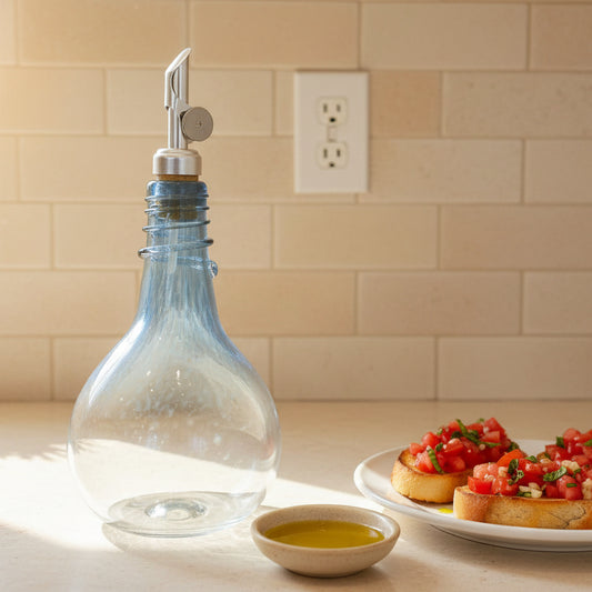 Clear glass Blue Spiral Oil drizzler bottle with blue spiral design and metal pour spout displayed with green potted plants