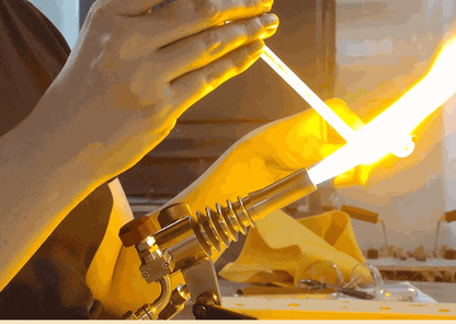 Hands shaping glass rod in bright flame at flameworking rental studio with professional torch setup