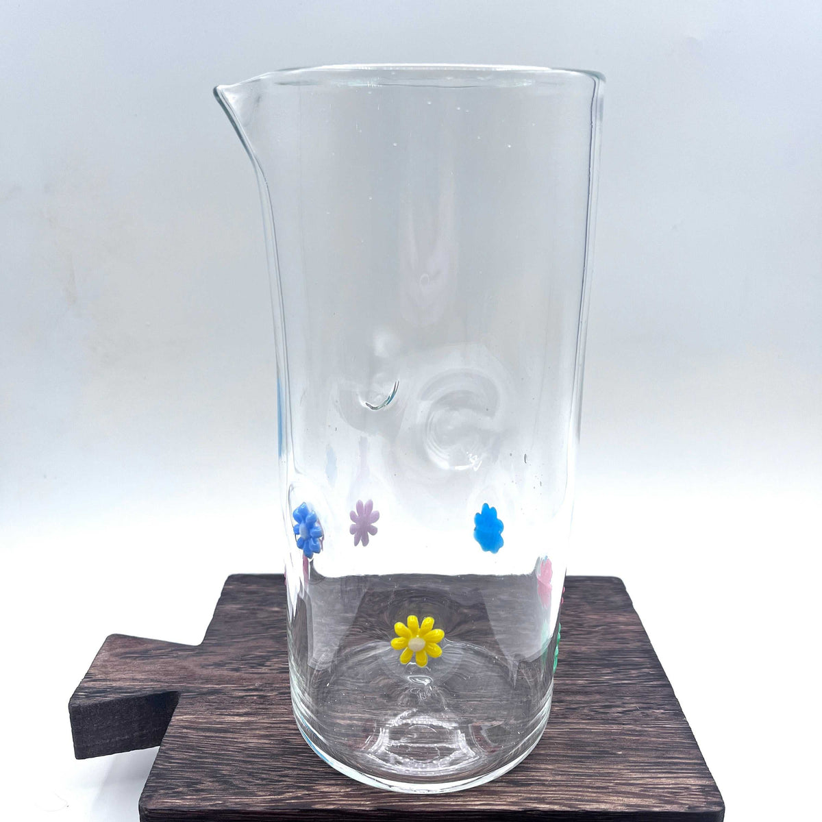 Hand blown stemless glass pitcher with colorful retro flower designs on clear glass
