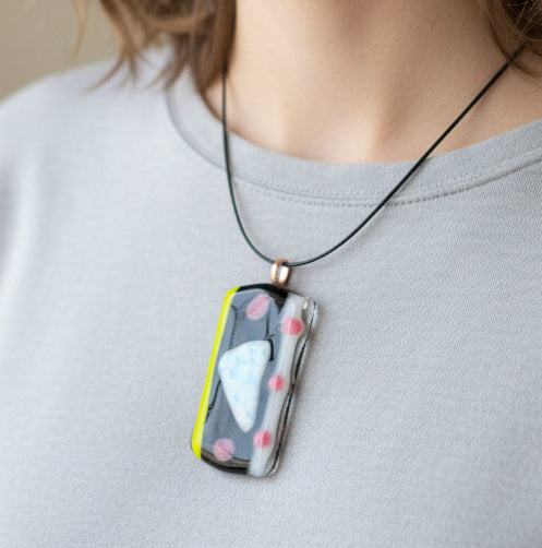 Neon green, pink, and black pendant on a necklace against a beige background