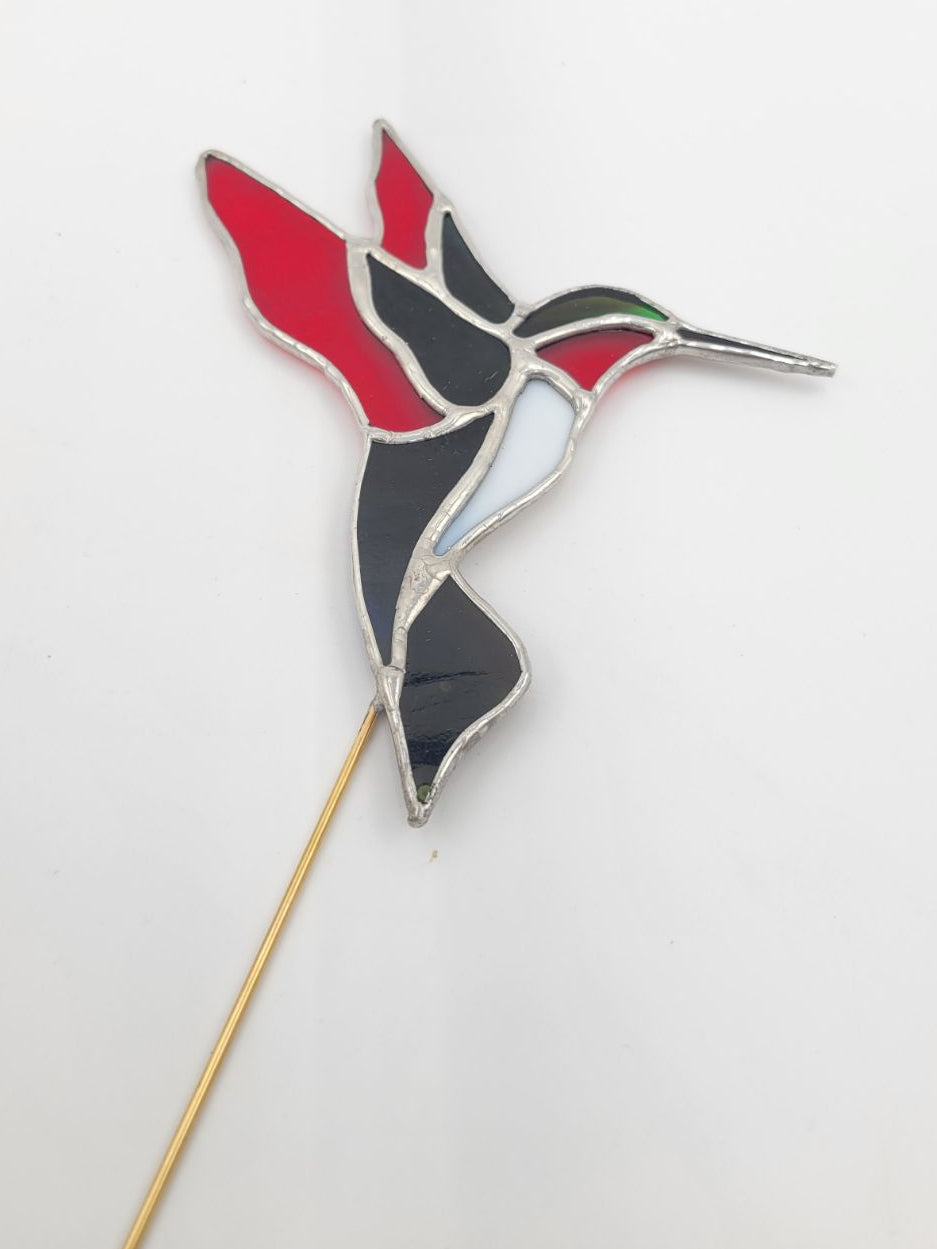 Decorative hummingbird on a stick with red, black, and white colors against a light gray background.