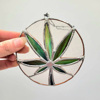 Hand holding a stained glass suncatcher with green leaf design on a white background
