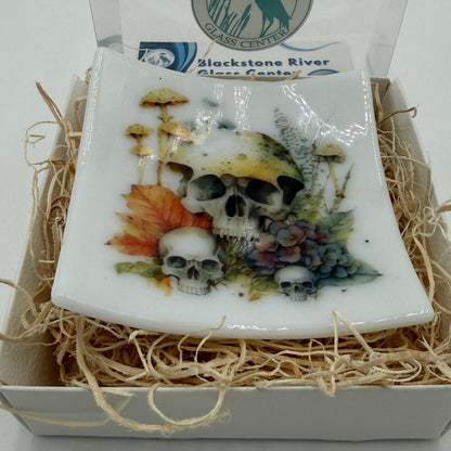 A square white glass  plate featuring a detailed graphic of skulls, mushrooms, autumn leaves, and grapes, presented in a gift box with shredded paper and a clear lid. The lid features the 'Blackstone River Glass  logo.