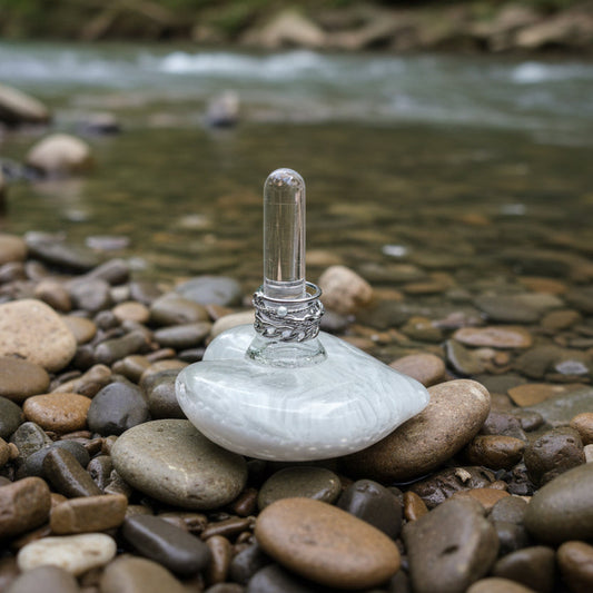 Clear glass ring holder with a silver ring on a white surface with white flowers in the background